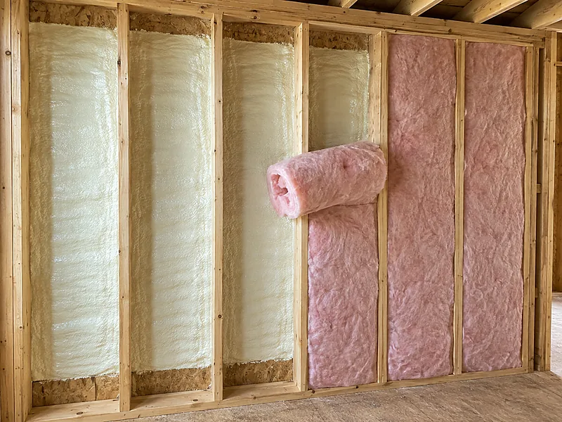 Fiberglass batt being installed over a closed-cell flash coat in a flash-and-batt wall assembly